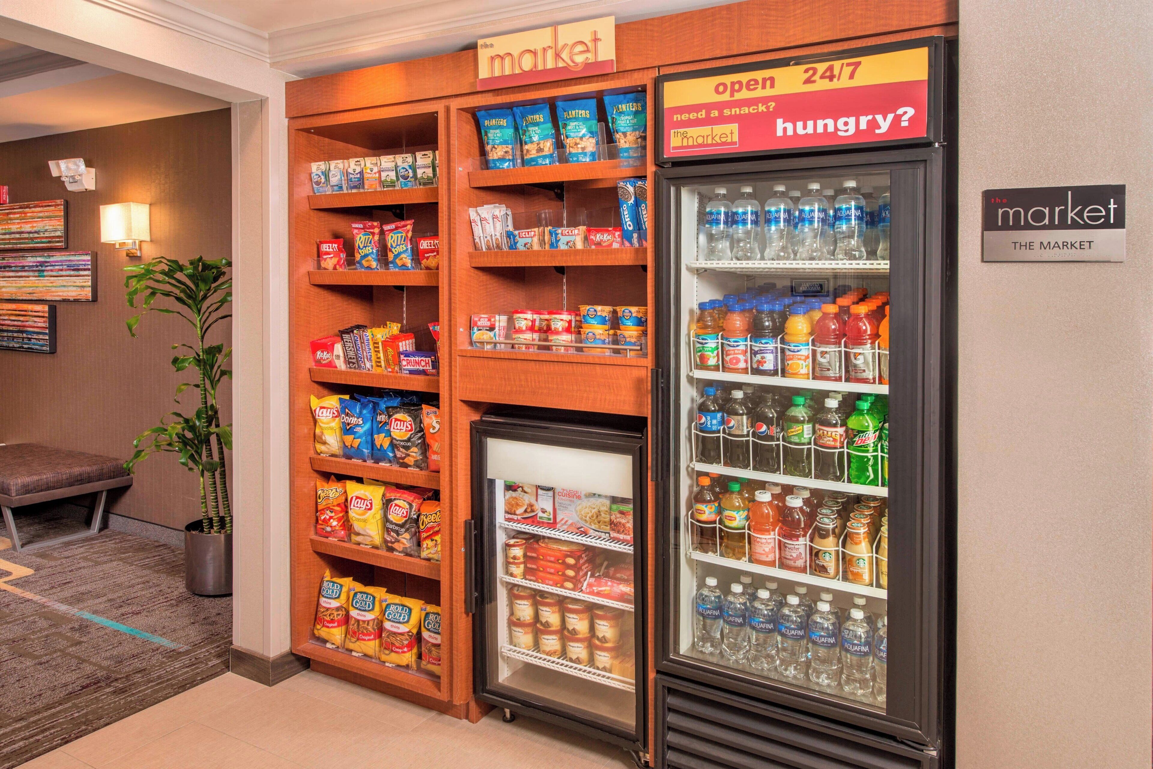 A hotel room with a small market area featuring snacks, drinks, and a refrigerator stocked with beverages.