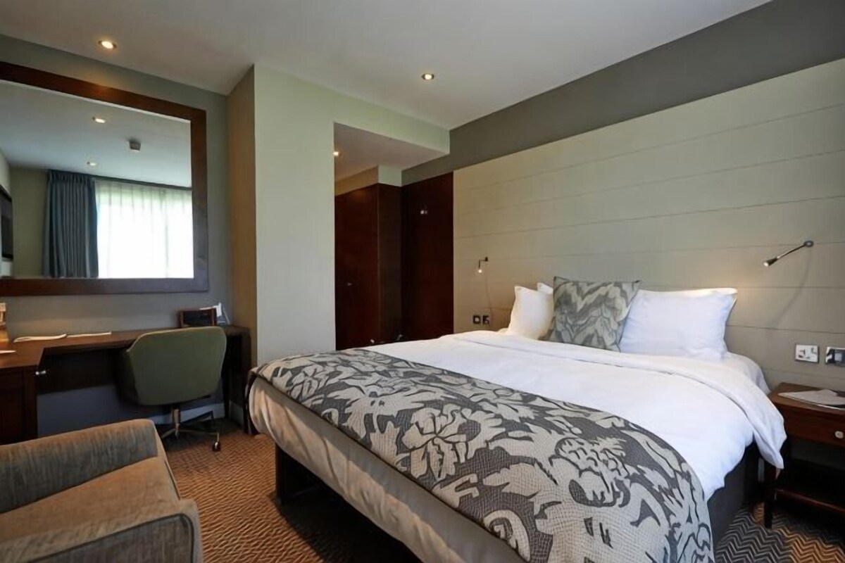 A hotel room with a bed, a desk, a chair, a mirror, and a nightstand.