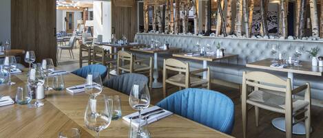 Un restaurante con mesas de madera, sillas tapizadas en azul y lámparas colgantes de mimbre.