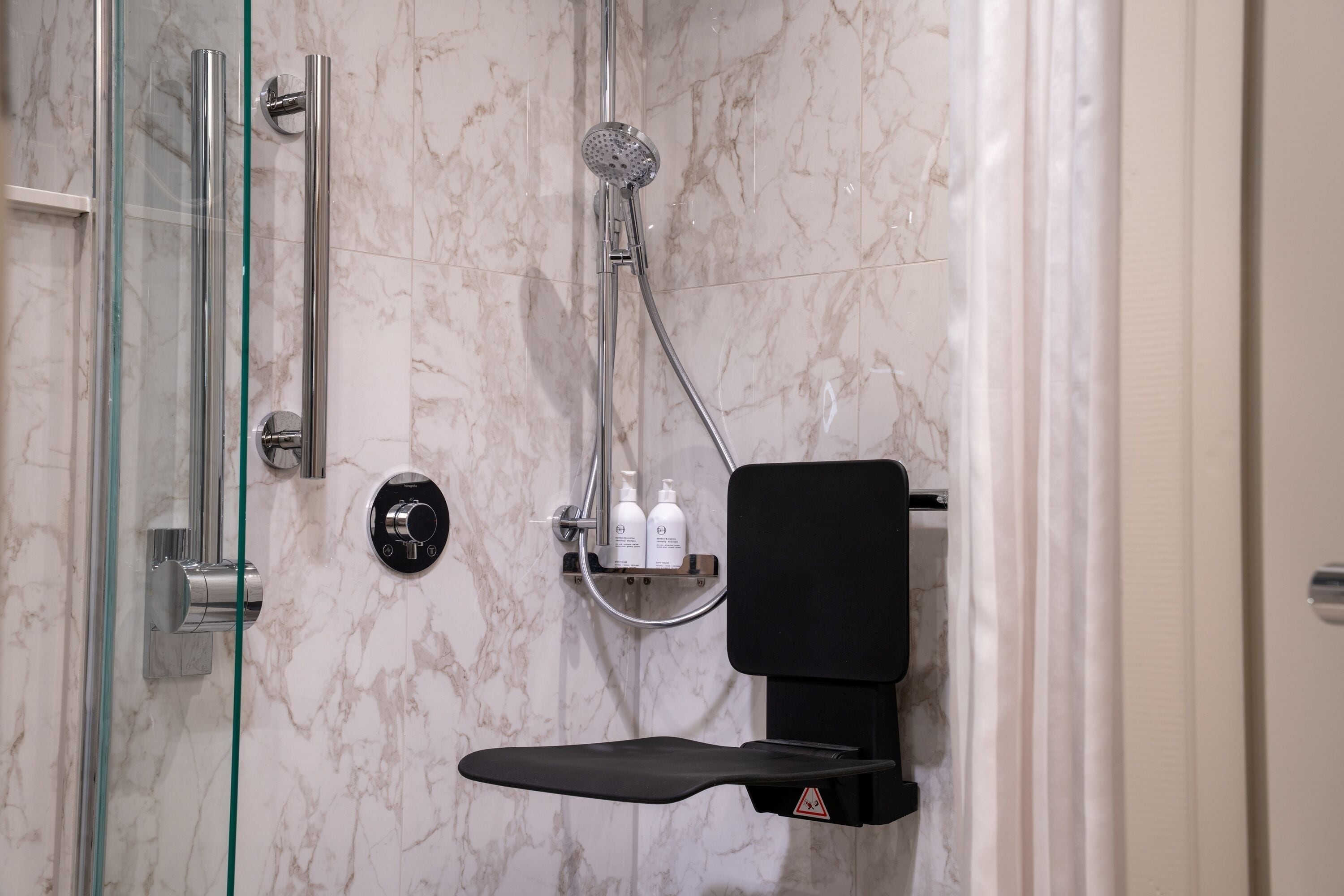 A modern bathroom with a glass-enclosed shower, a black seat, and a marble wall.
