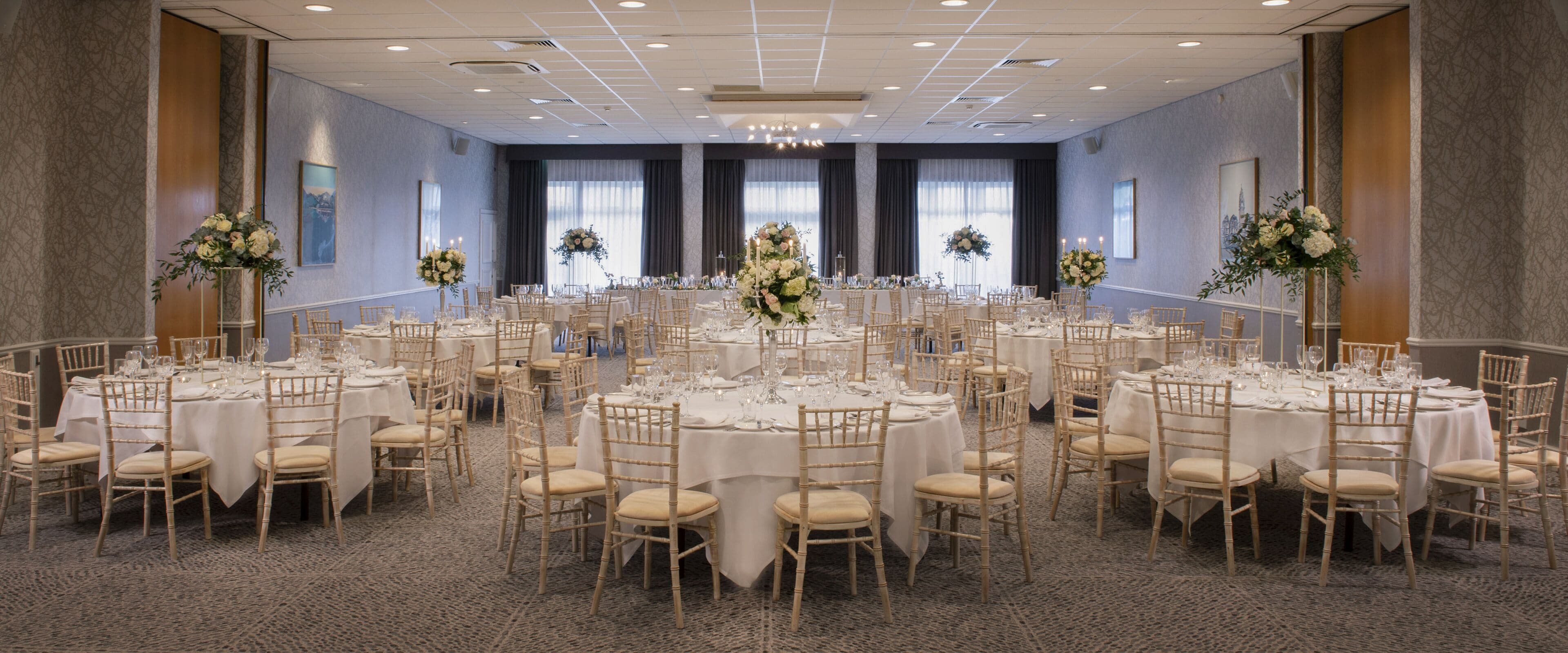 A large banquet hall with round tables, white tablecloths, and floral centerpieces.
