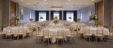 Un gran salón de banquetes con mesas redondas, manteles blancos y centros de mesa florales.