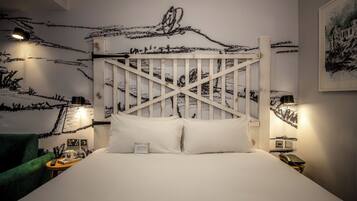 A hotel room with a white bed, a wooden headboard, a green armchair, bedside tables with lamps, and a wall with a black and white abstract design.
