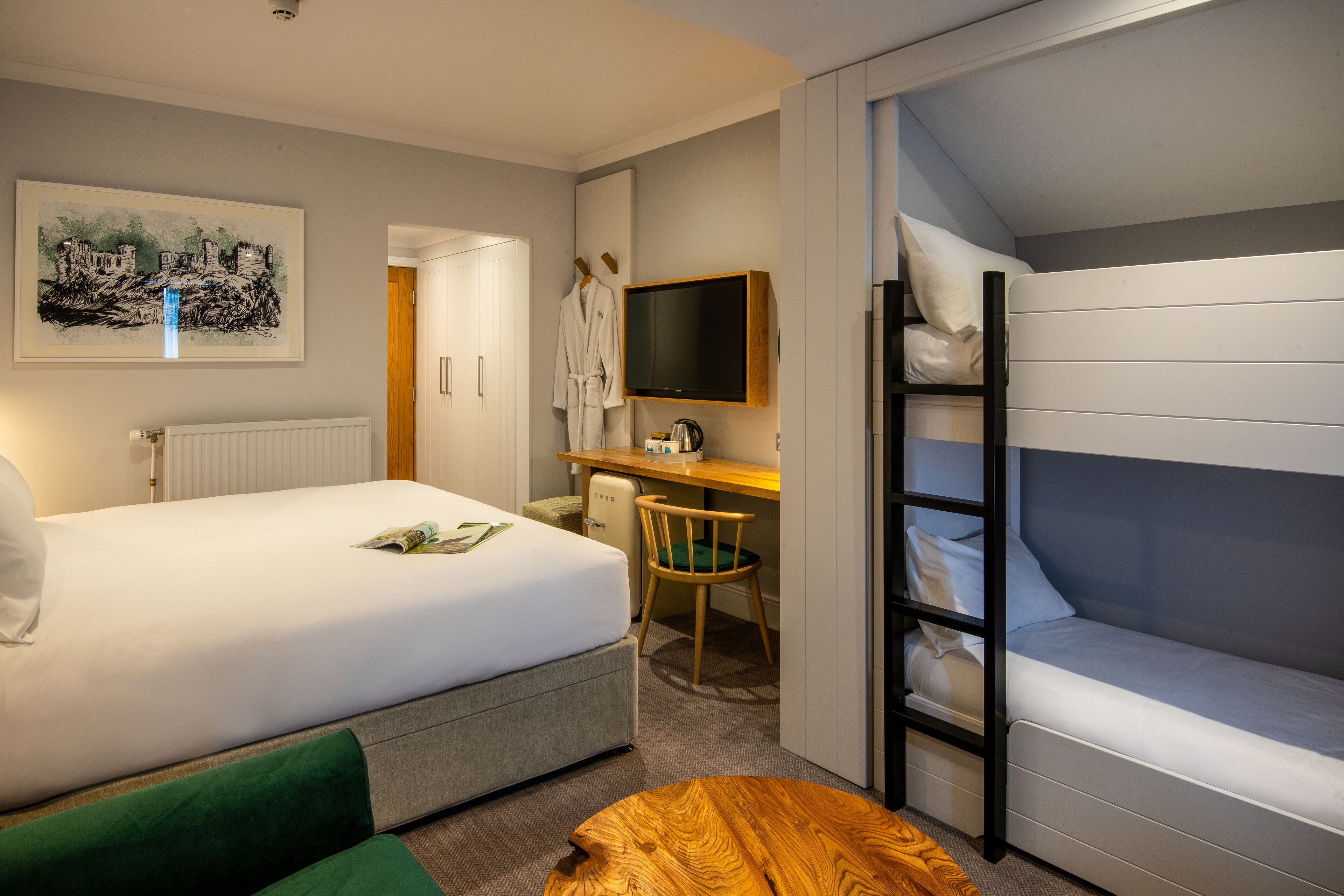 A hotel room with a bed, a desk, a chair, a TV, and a bunk bed.