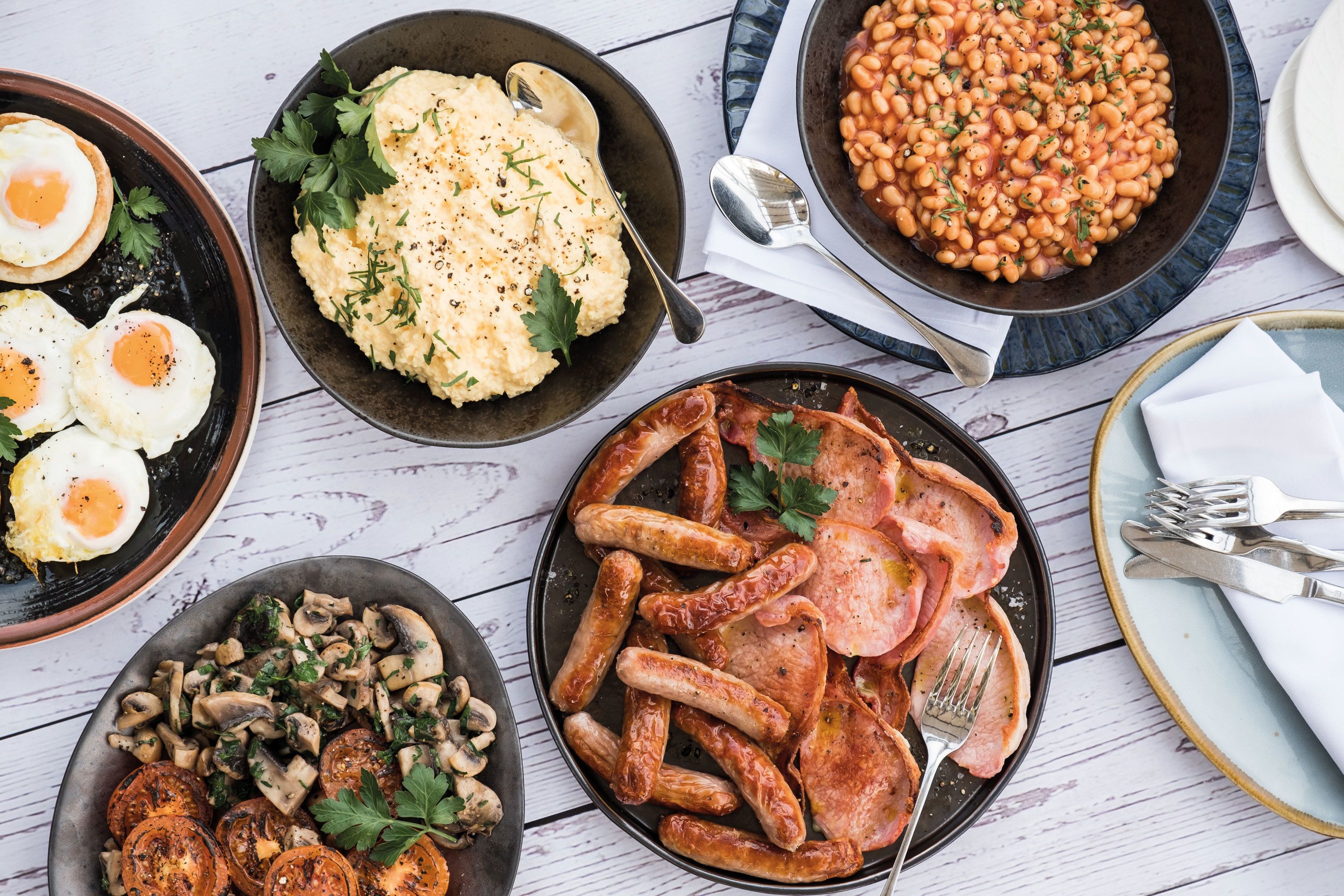 Variedad de platos que incluyen huevos, puré de papas, frijoles, salchichas y champiñones.