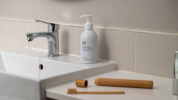 A bathroom sink with a bottle of shampoo and two wooden toothbrushes on the counter.
