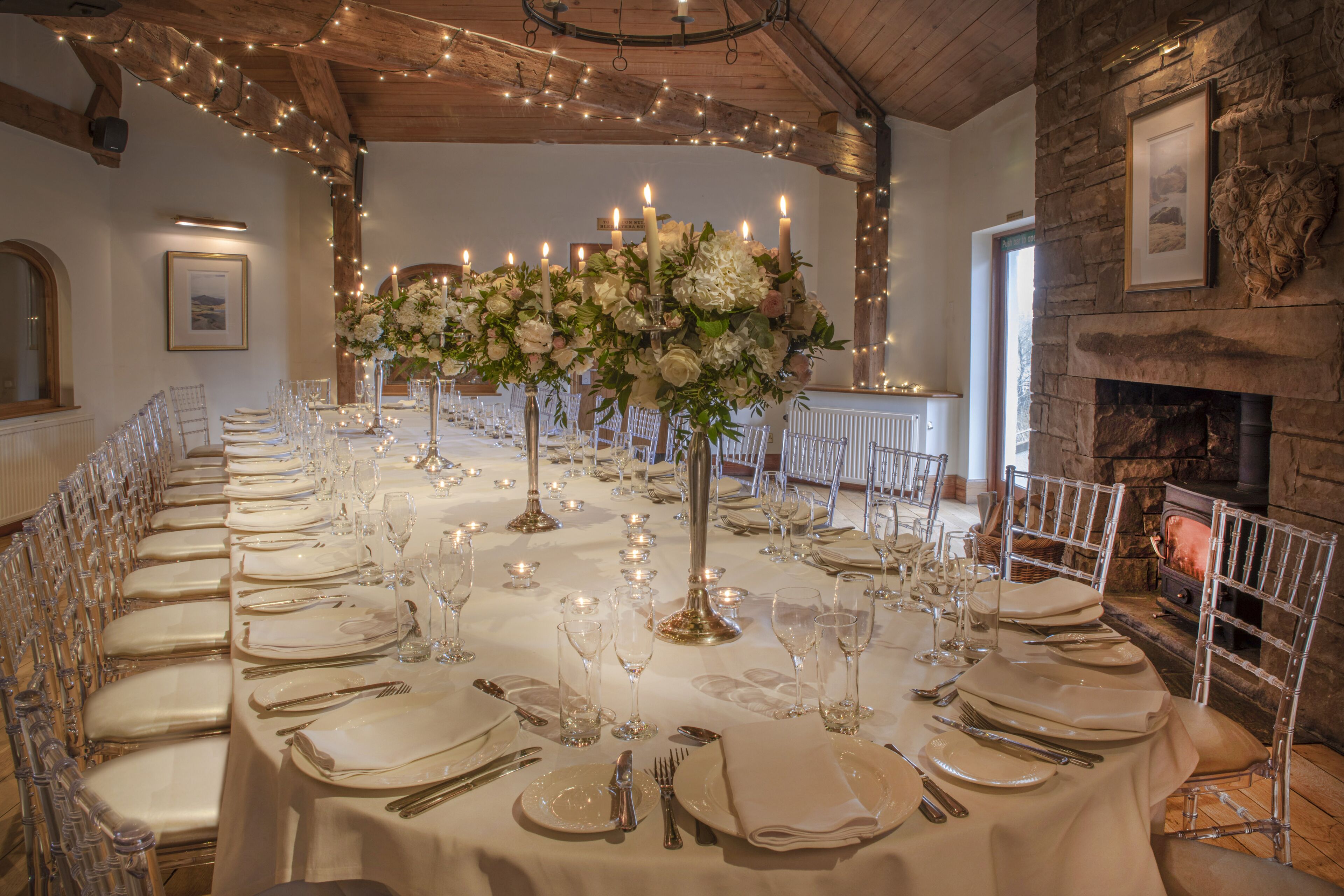 A long banquet table set for a formal event, with candles, glassware, and clear chairs.