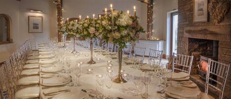 A long banquet table set for a formal event, with candles, glassware, and clear chairs.