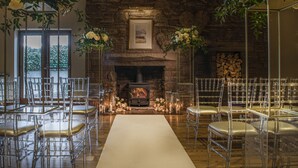 Un lieu de réception pour mariages doté d’une cheminée en pierre, de chaises transparentes et de compositions florales.