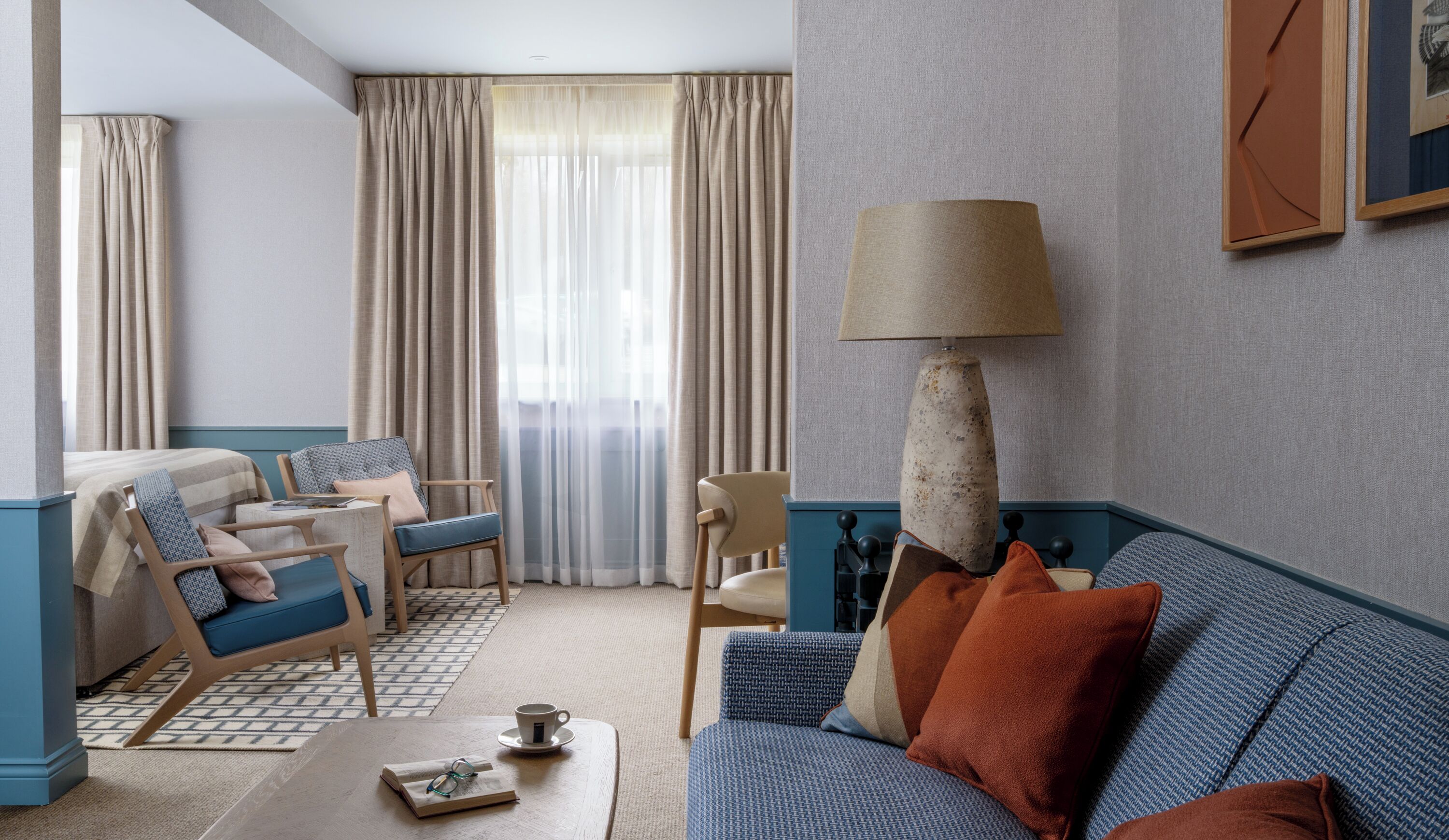 A hotel room with a bed, two chairs, a sofa, a coffee table, and a lamp.