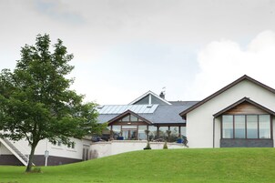 A modern building with a sloped roof, a staircase leading to a door, and a grassy hill in the foreground.