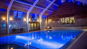 Une piscine intérieure avec des poutres en bois au plafond, un espace détente et des tableaux encadrés accrochés aux murs.