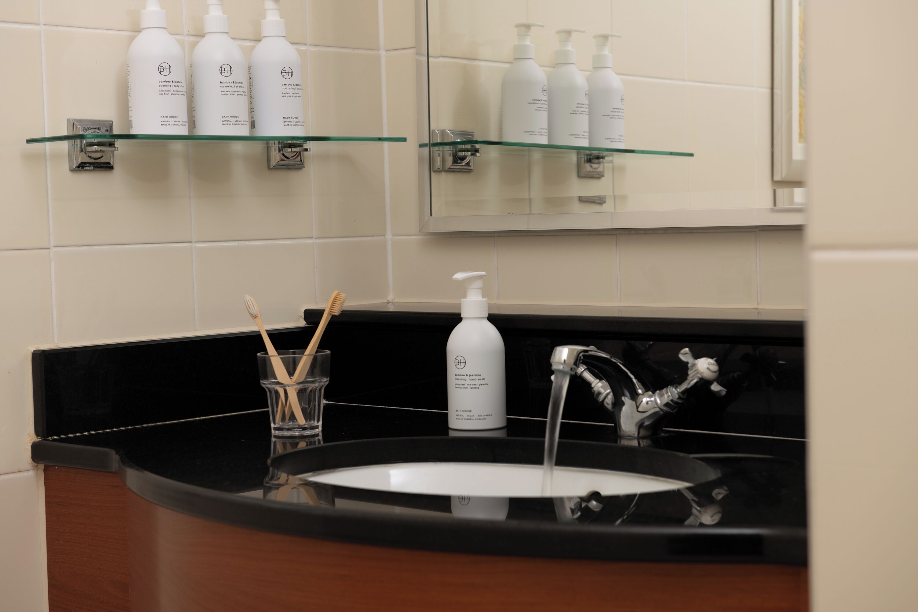 A bathroom with a black countertop, a white sink, and a mirror above it. There are shelves with white bottles and a toothbrush holder with toothbrushes.
