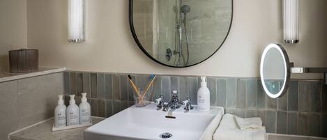 A bathroom with a white sink, a mirror, and a shower. There are toiletries on the sink and a towel on the counter.