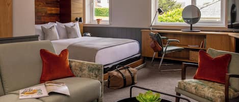 Ett hotellrum med en säng, en soffa, ett skrivbord och ett fönster med utsikt över grönområden.