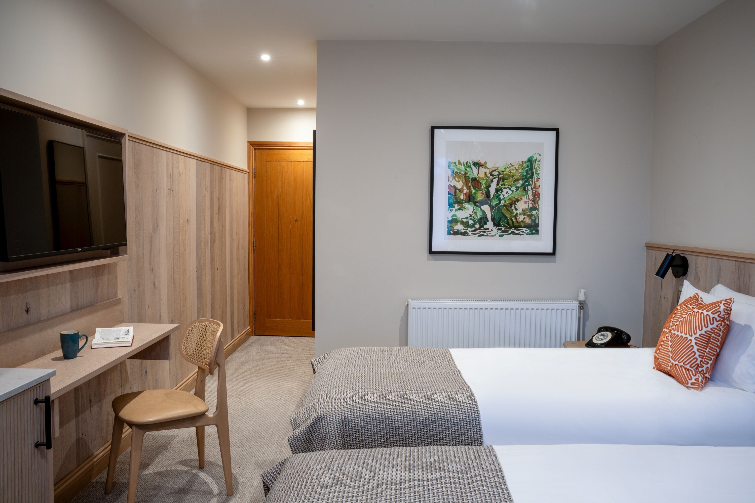 A hotel room with a bed, a desk with a chair, a television, and a framed picture on the wall.