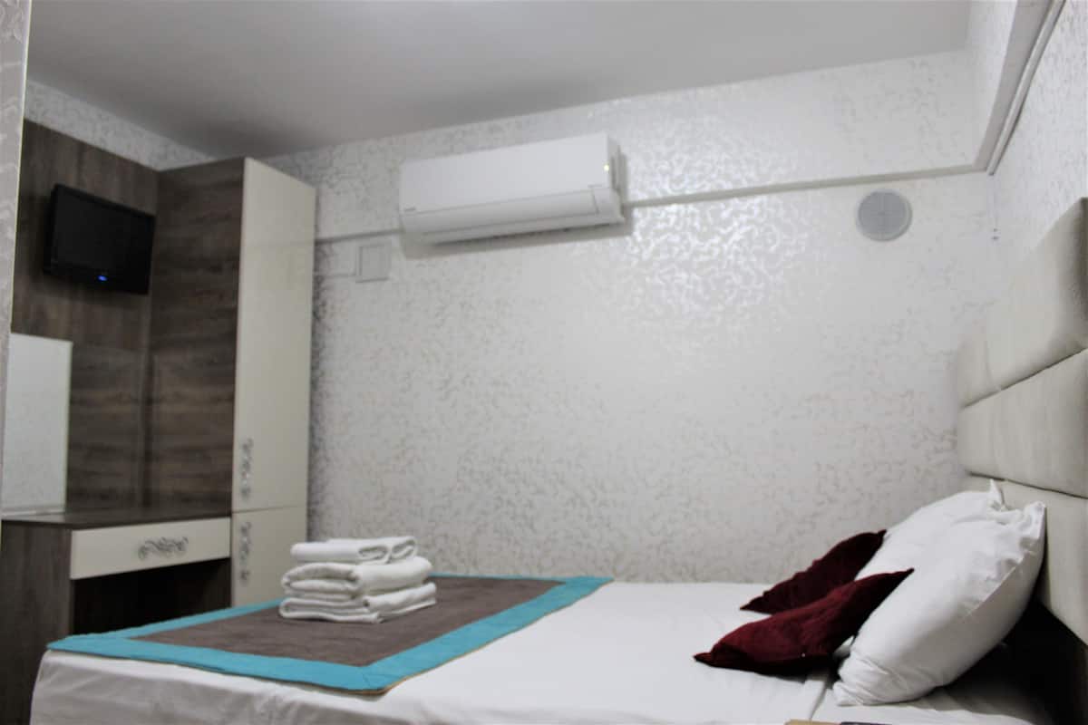 Een hotelkamer met een bed, een aan de muur bevestigde televisie en een luchtverkoeler.