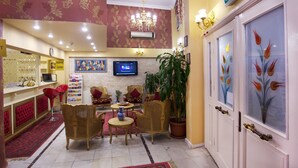 A hotel lobby with a reception desk, seating area with chairs and tables, a television, and a potted plant. - Divas Hotel (Istanbul)