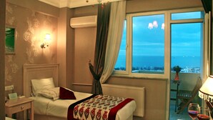A hotel room with a bed, a nightstand, a chair, a table with a lamp, and a view of the sea. - Divas Hotel (Istanbul)