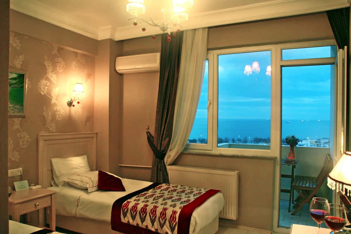 Een hotelkamer met een bed, een nachtkastje, een stoel, een tafel met een lamp, en uitzicht op de zee.
