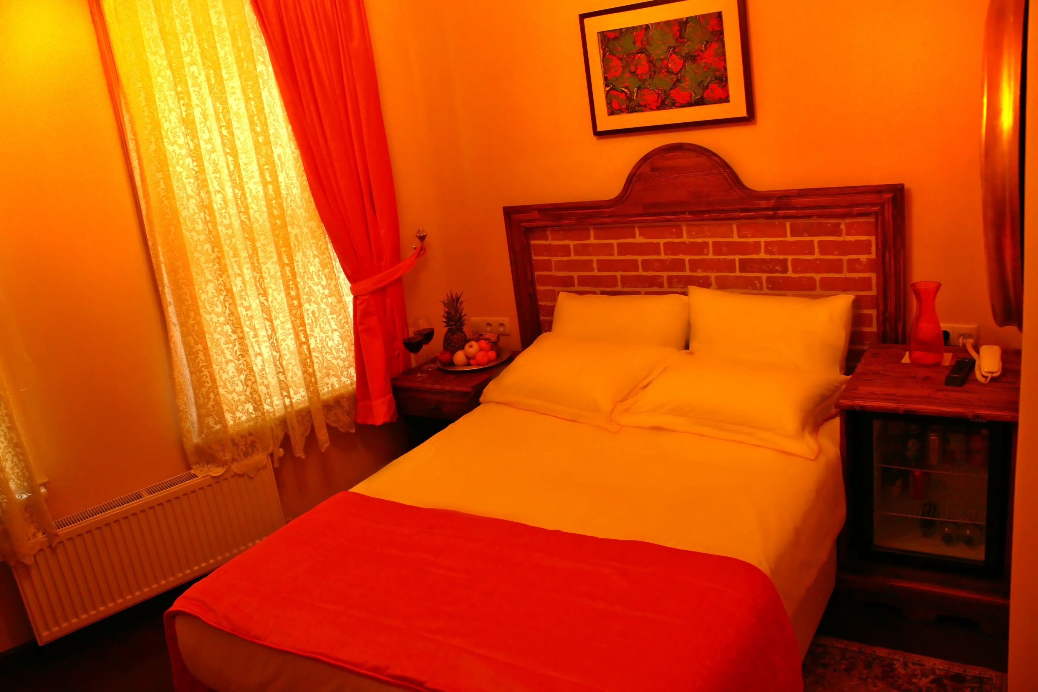A hotel room with a brick headboard, a bed with white bedding, a nightstand with a lamp, and a framed picture on the wall.