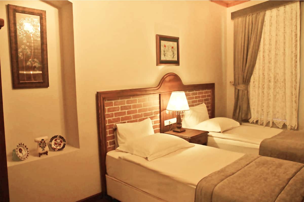 Een hotelkamer met twee bedden, een nachtkastje met een lamp, een bakstenen muur en een ingelijst schilderij aan de muur.