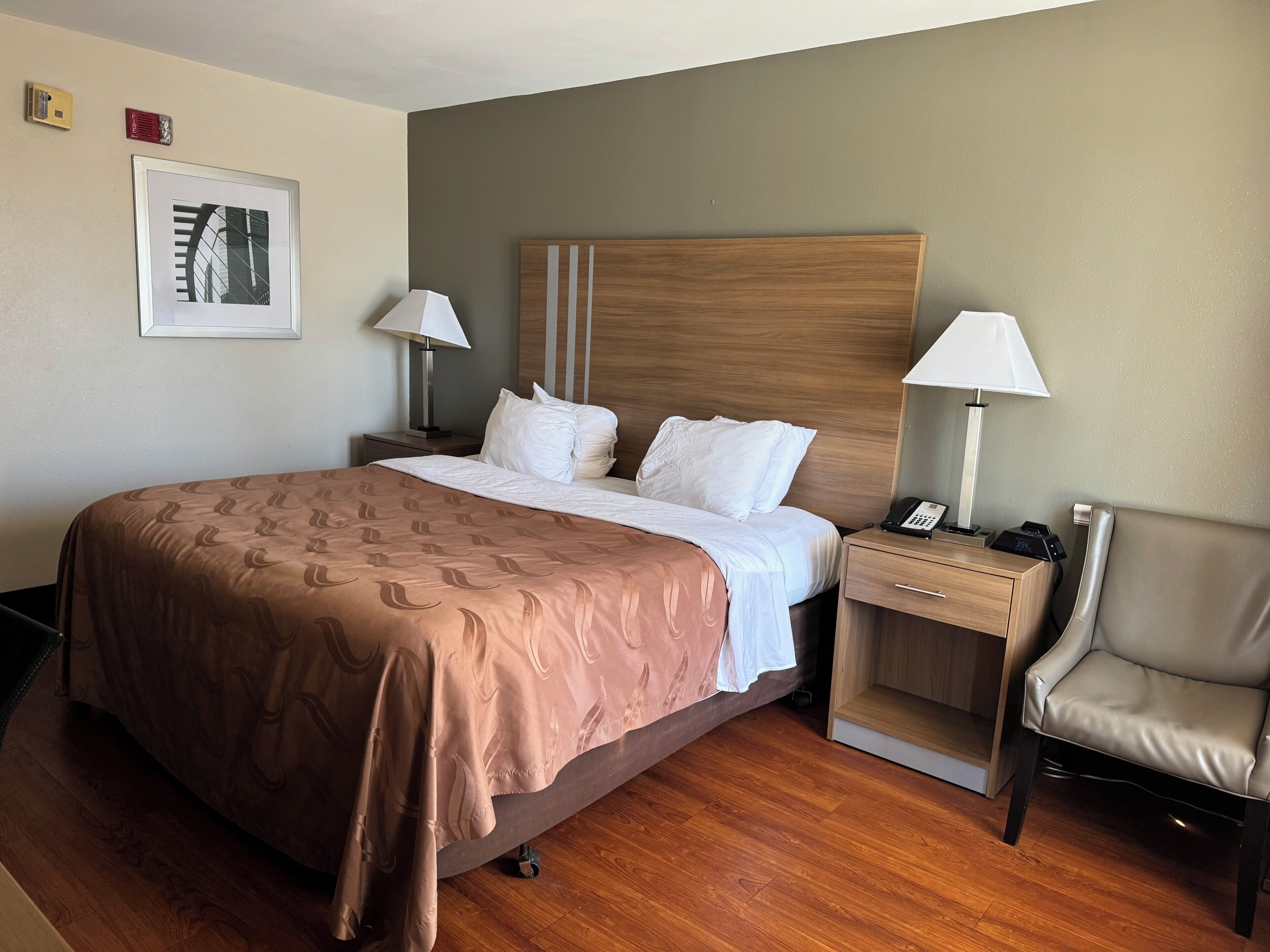 A hotel room with a large bed, two bedside tables with lamps, a chair, and a framed picture on the wall.