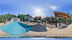 Una piscina con un toldo, sillas de descanso y una zona de estar cubierta.