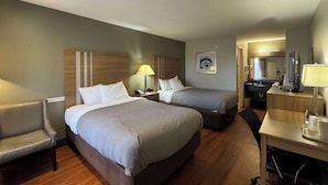 Habitación de hotel con dos camas, un escritorio, una silla, un televisor y un baño visible a través de una puerta abierta.