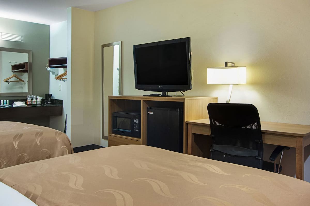 Una habitación de hotel con una cama, un escritorio con computadora, televisor, microondas y refrigerador.