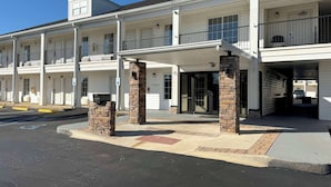 Un hotel de varios pisos con entrada cubierta, pilares de piedra y un estacionamiento con espacios reservados para discapacitados.