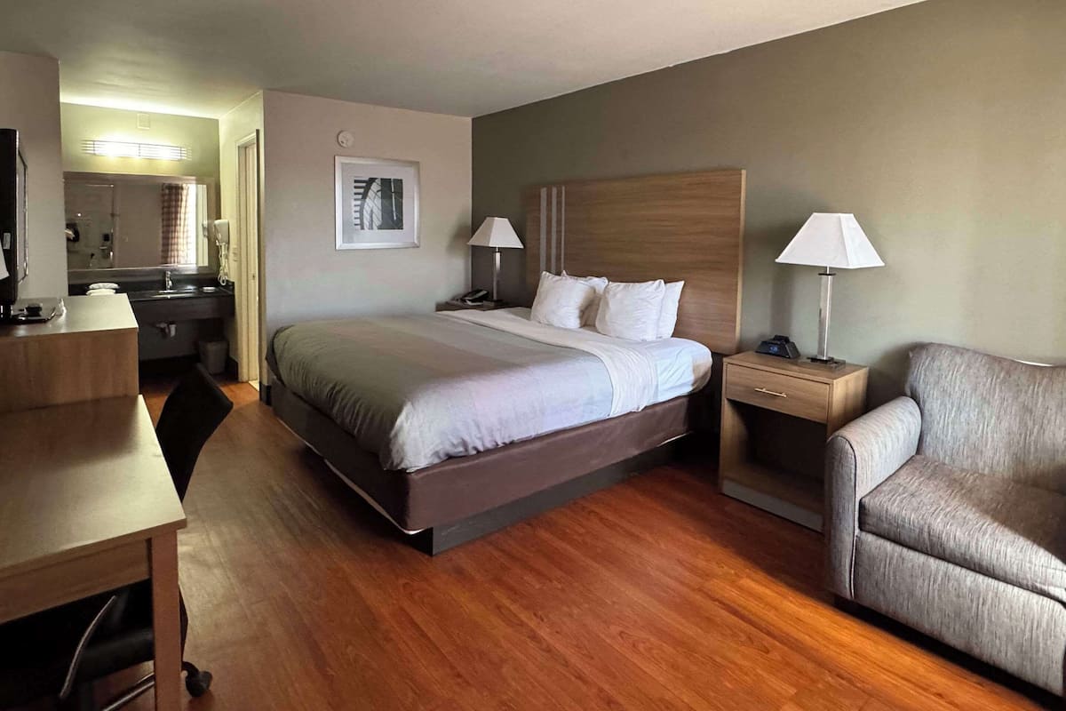 Habitación de hotel con una cama grande, mesitas de noche, un escritorio, una silla y un baño a la vista.