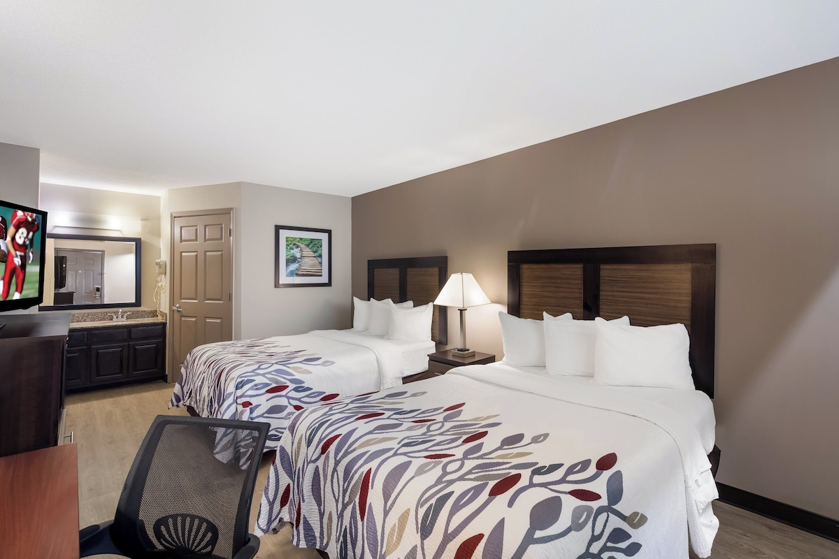 A hotel room with two beds, a desk, a TV, and a bathroom.