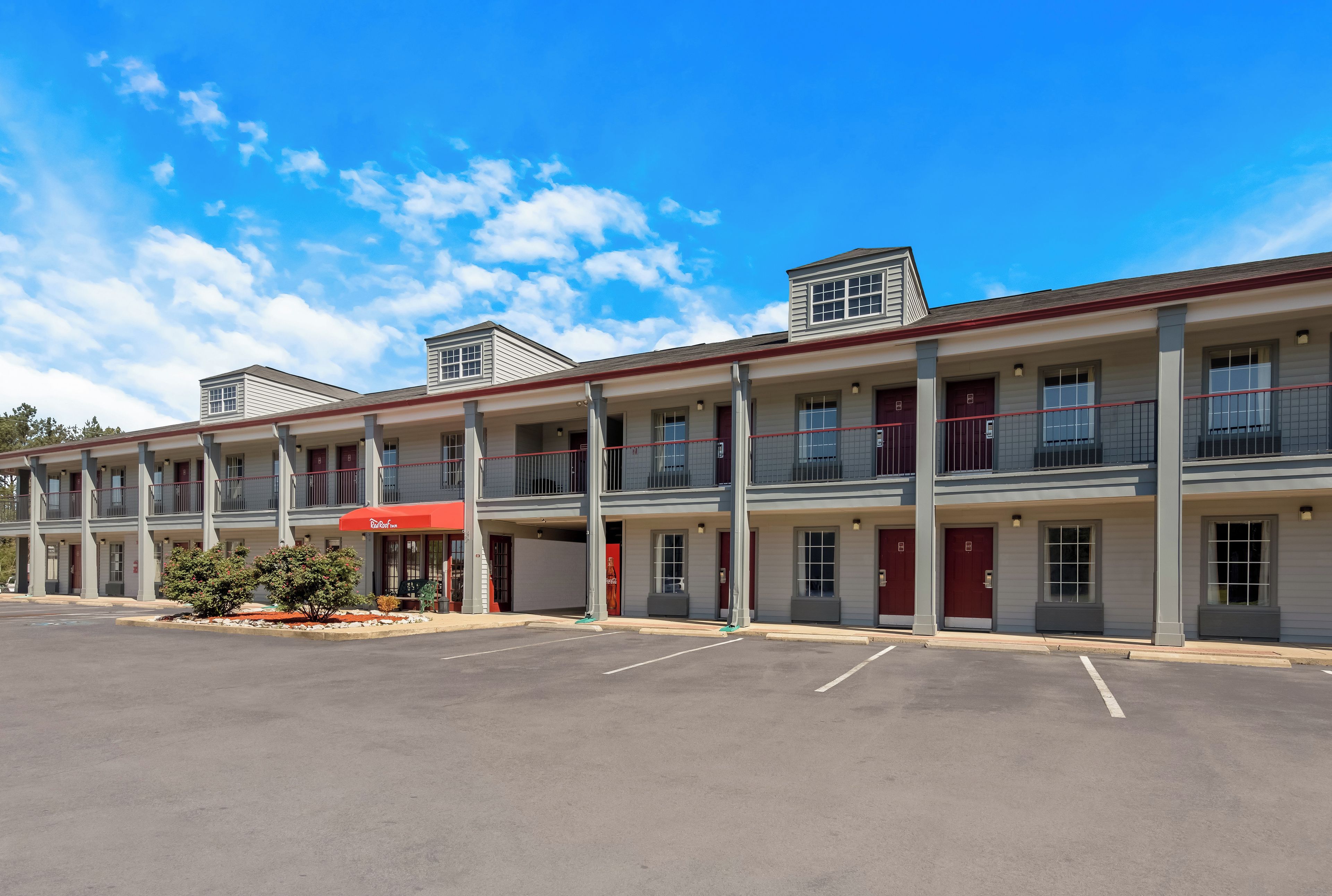 A motel with a red awning, multiple balconies, and a parking lot.