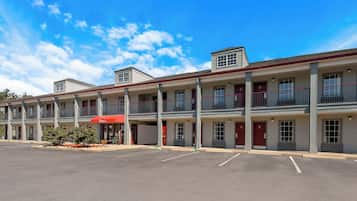 A motel with a red awning, multiple balconies, and a parking lot.