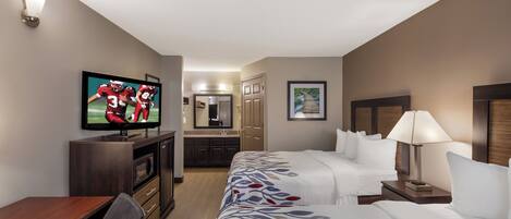 A hotel room with a TV, a desk, a bed, a nightstand, and a bathroom visible through an open door.