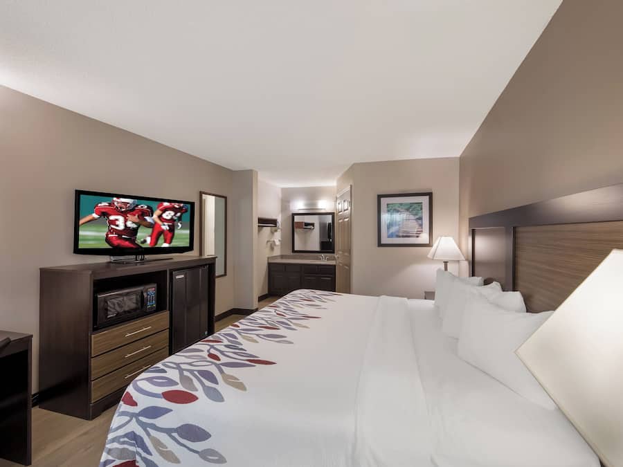 A hotel room with a bed, a television, a desk with a computer, and a bathroom visible in the background.