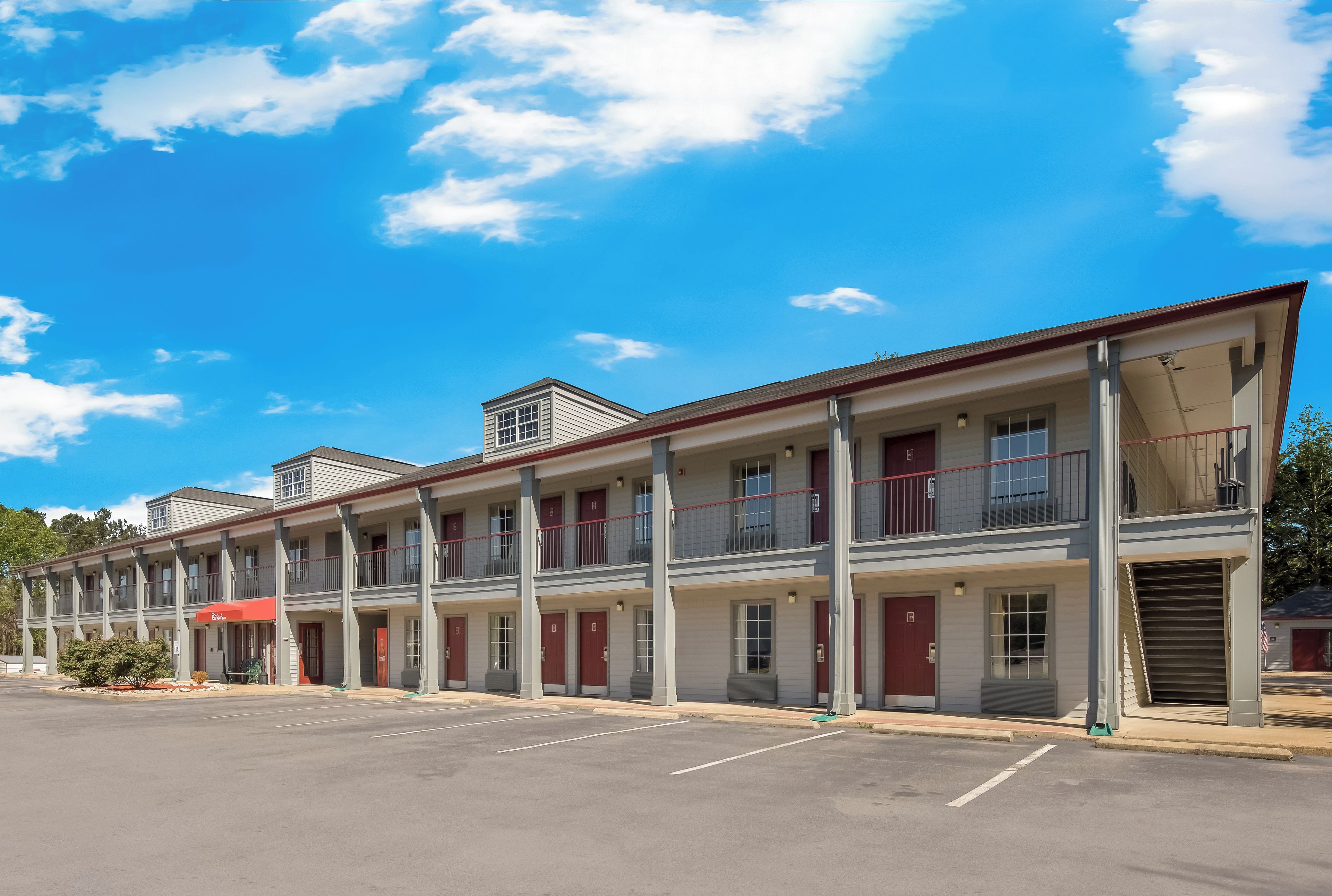 Una hilera de edificios de motel con varios pisos y balcones, un estacionamiento al frente y un cielo azul despejado.