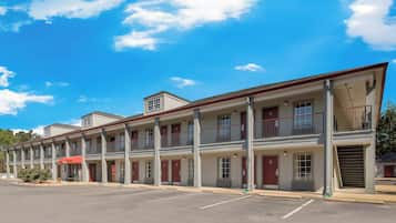 Una hilera de edificios de motel con varios pisos y balcones, un estacionamiento al frente y un cielo azul despejado.