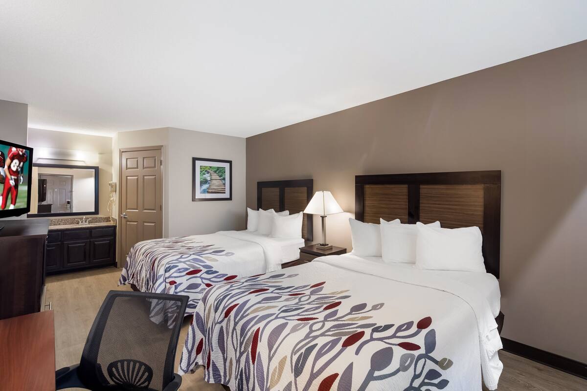 Quarto de hotel com duas camas, uma escrivaninha, televisão e banheiro.
