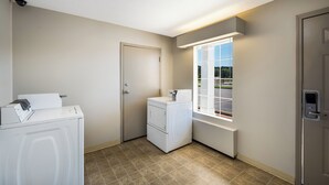 Un cuarto de lavado con lavadora, secadora y ventana con vista a un estacionamiento.