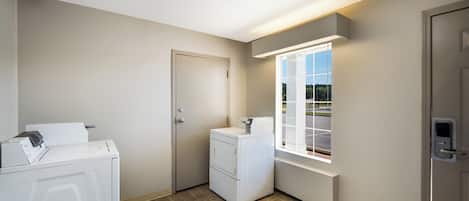 A laundry room with a washing machine, dryer, and a window with a view of a parking lot.