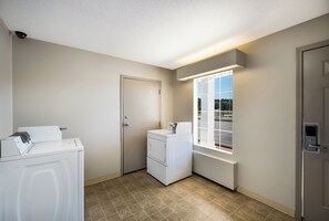 A laundry room with a washing machine, dryer, and a window with a view of a parking lot. - Red Roof Inn Jasper (Jasper)
