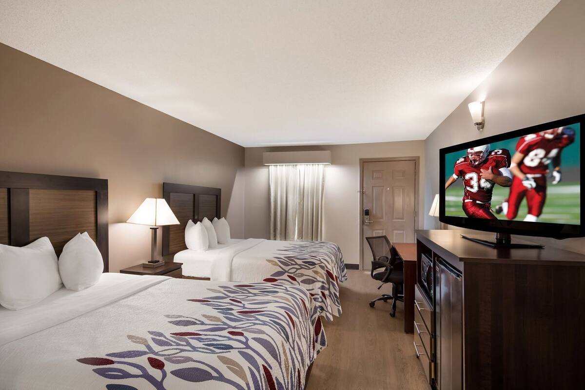 Quarto de hotel com duas camas, televisão, escrivaninha e uma cadeira.