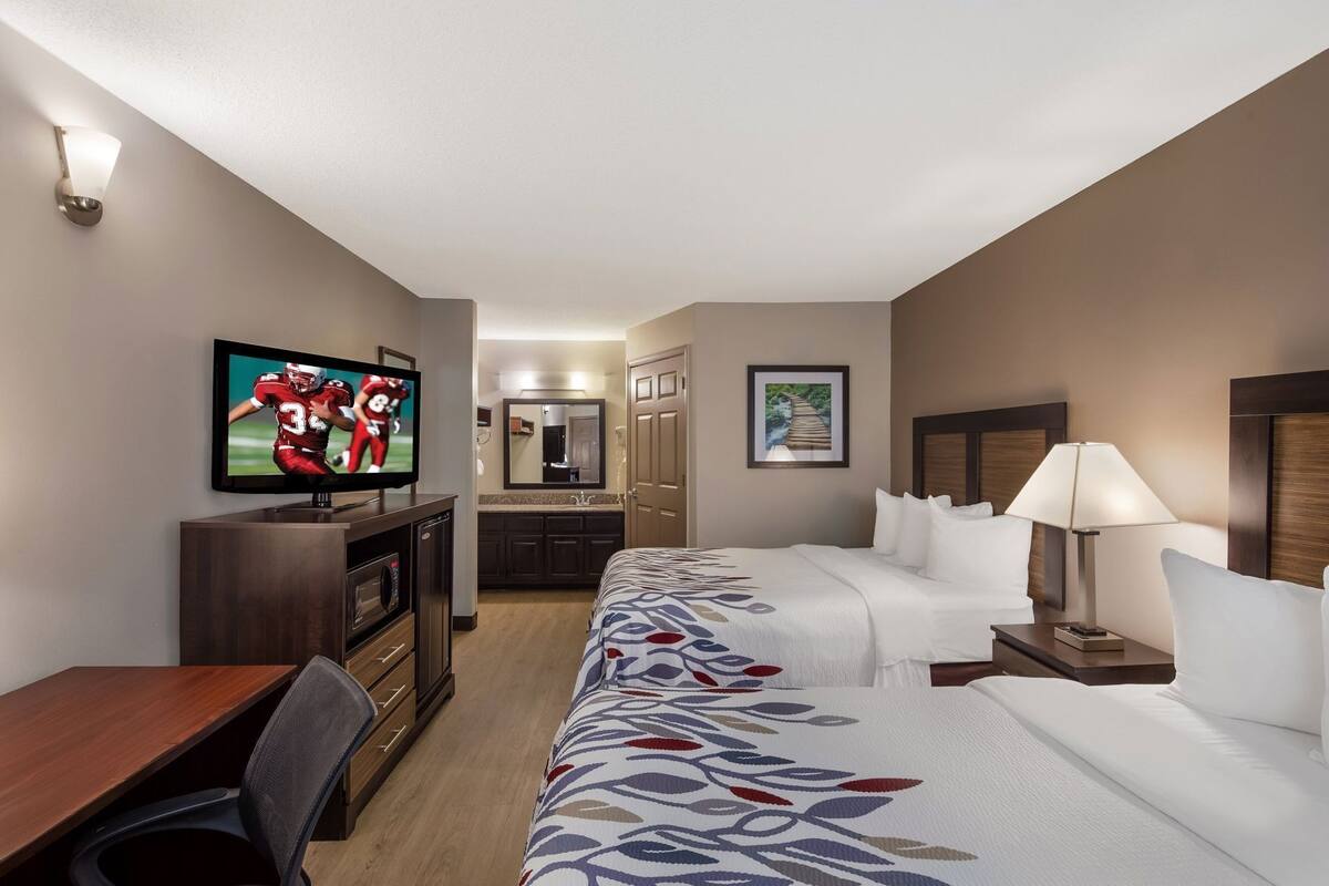 Quarto de hotel com televisão, secretária, cama, mesa de cabeceira e banheiro.