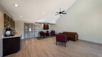 A spacious room with a kitchen area, a seating area with a sofa and chairs, a ceiling fan, and a stone wall.