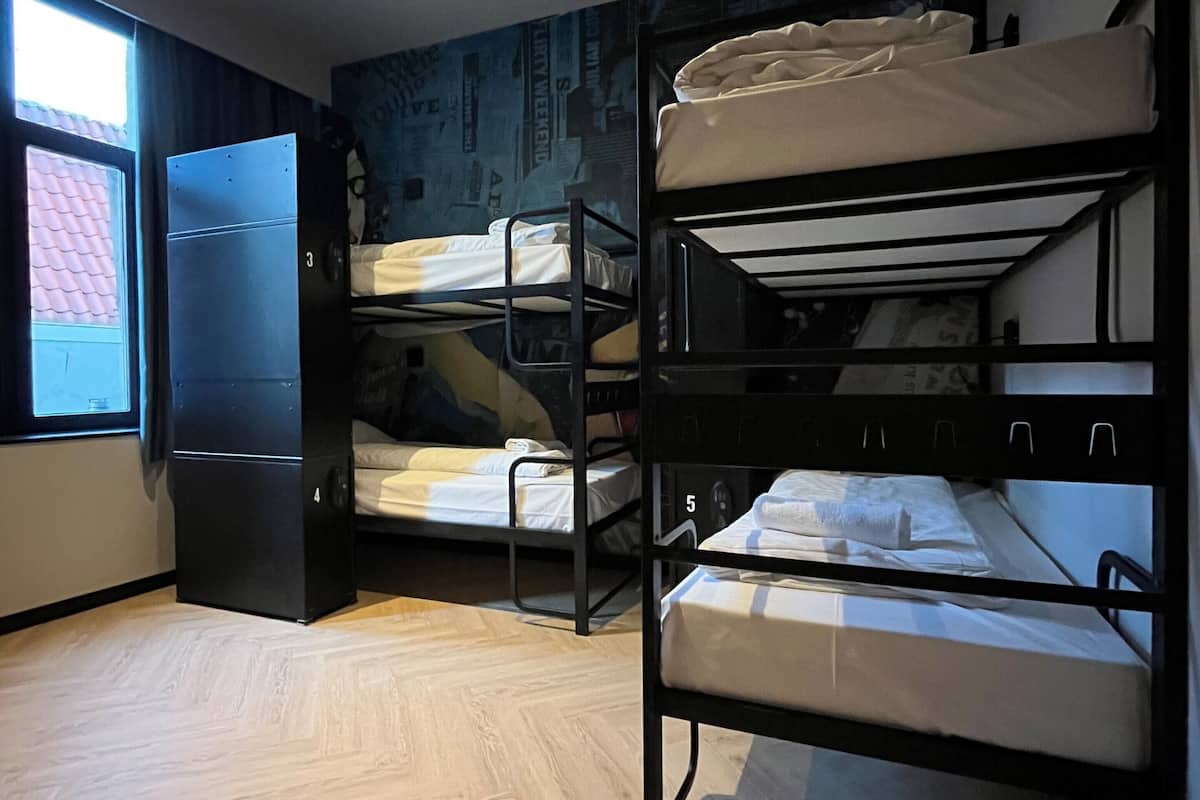 A dormitory room with bunk beds, a window, and a wall with a cityscape mural.