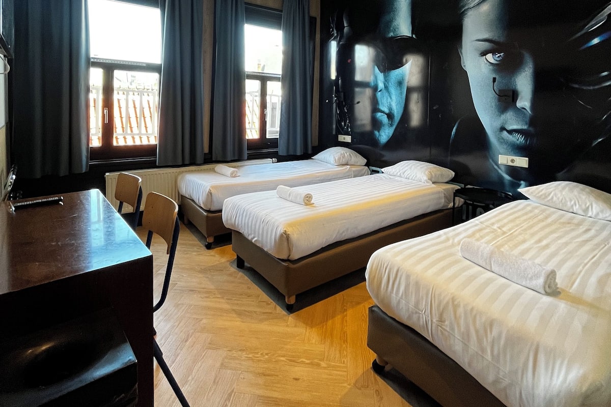 A hotel room with three beds, a desk, and a large mural on the wall.