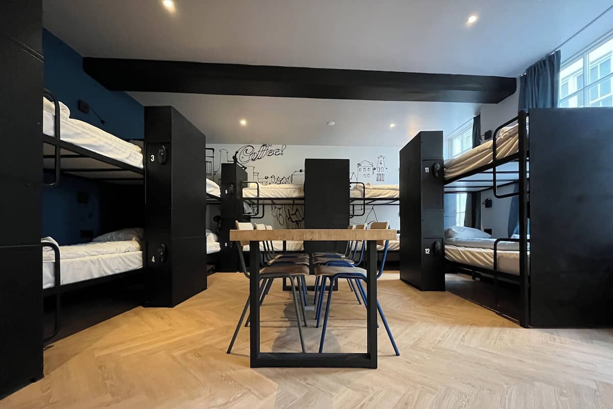 A bunk bed room with a wooden floor, a table with chairs, and a wall with a coffee-themed mural.