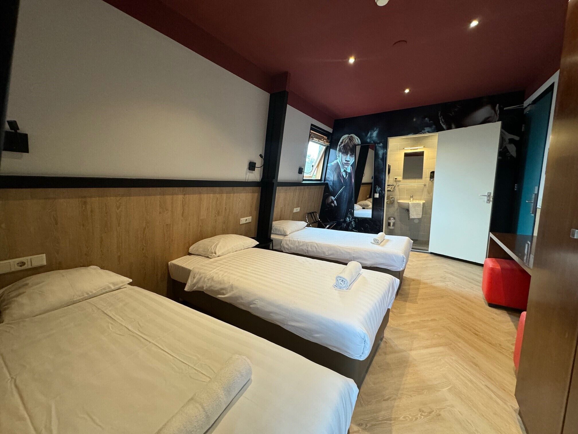 Ein Hotelzimmer mit drei Einzelbetten, einem Holzkopfende, einem großen Spiegel und einem Kleiderschrank.